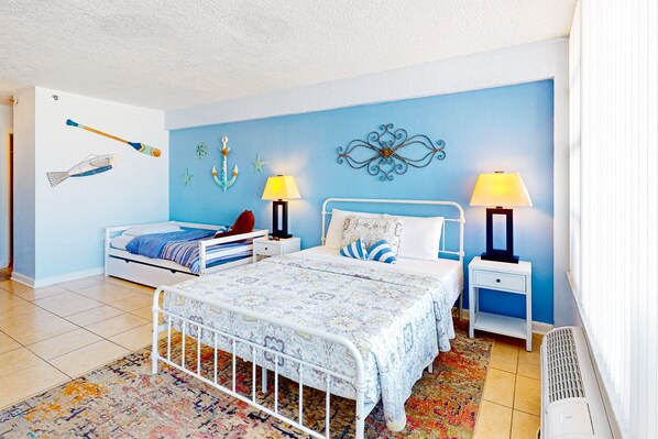 Une chambre à coucher comprenant un lit, deux tables de chevet, une commode, un radiateur, un mur décoré et une fenêtre.
