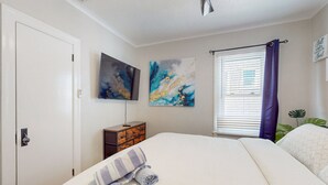 A bedroom with a bed, a dresser, two paintings, a window with blinds, and a potted plant. - Daytona Beach Retreat (Daytona Beach)