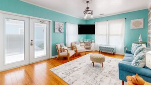A living room with teal walls, a wooden floor, a blue sofa, two armchairs, a coffee table, and a chandelier. - Daytona Beach Retreat (Daytona Beach)