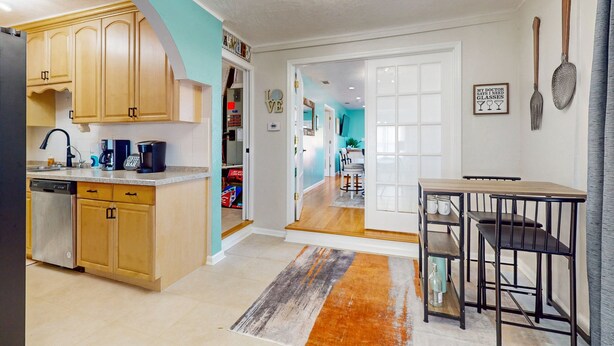 A modern kitchen with wooden cabinets, a dishwasher, and a coffee maker. There is a dining area with a table and chairs. - Daytona Beach Retreat (Daytona Beach)