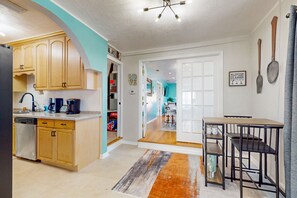 A modern kitchen with wooden cabinets, a dishwasher, and a coffee maker. There is a dining area with a table and chairs. - Daytona Beach Retreat (Daytona Beach)