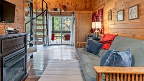 Un intérieur de chalet chaleureux, avec un revêtement mural en bois, un canapé, un téléviseur et une cheminée.