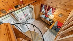 L’intérieur d’un chalet en bois comprend un escalier en colimaçon, un coin repas avec une table et des chaises, et une fenêtre avec des rideaux.