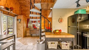 Un intérieur en bois comprenant un espace cuisine avec une table en bois, un réfrigérateur en acier inoxydable et des paniers en osier.