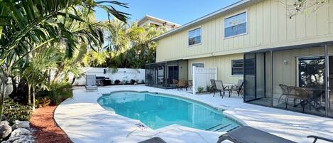 A backyard with a swimming pool, patio furniture, and a covered seating area.