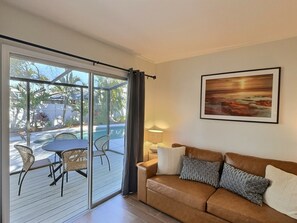Quarto com porta de vidro deslizante para área externa com piscina, um sofá com almofadas estampadas e um quadro na parede.