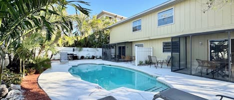 A backyard with a swimming pool, patio furniture, and a covered seating area.