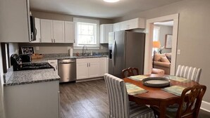 A modern kitchen with white cabinets, a stainless steel refrigerator, a built-in oven, and a dining area with striped chairs and a wooden table. - Historic Home in Downtown Greer Shop,eat & Sleep (Greer)