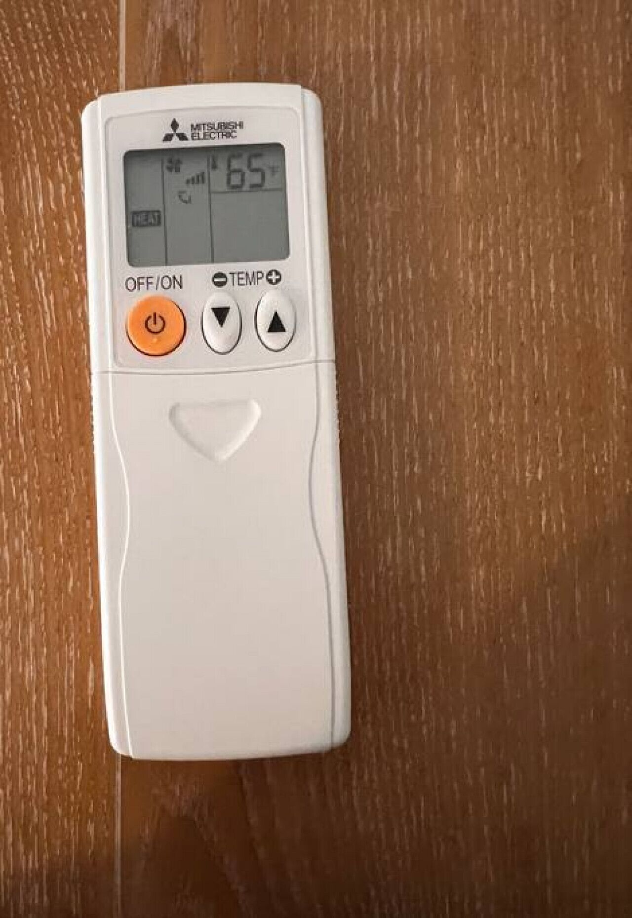 A white Mitsubishi Electrica thermostat with a digital display, OFF/ON switch, and TEMP+ buttons on a wooden surface.