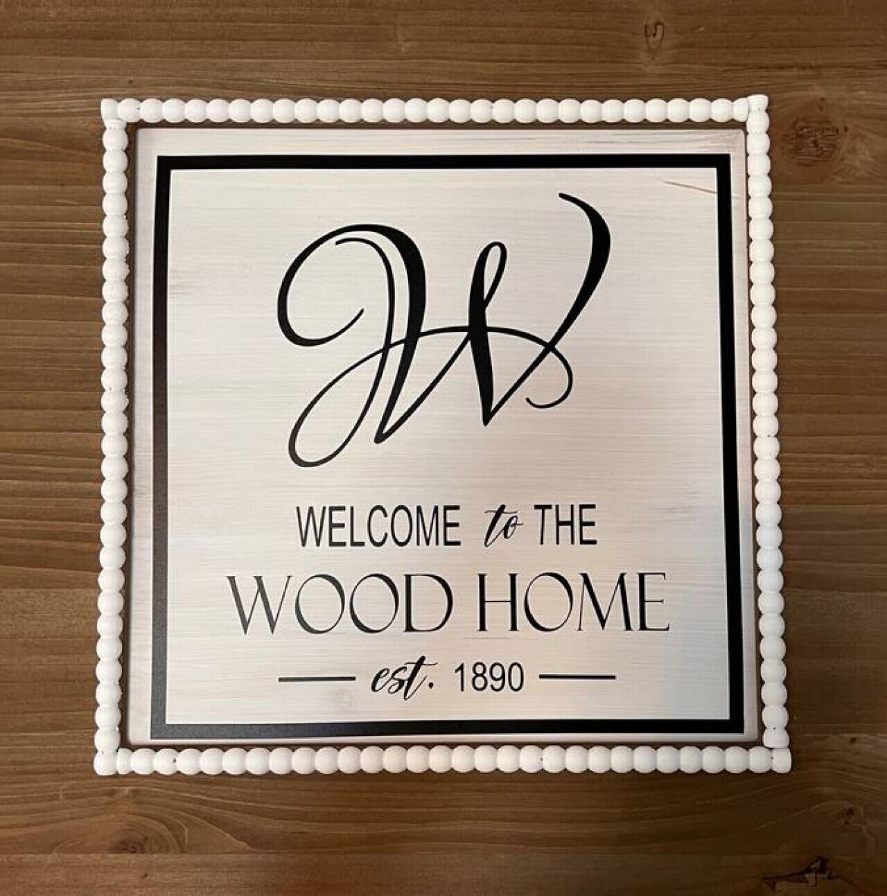 A welcome sign with a wooden border and a decorative bead trim, stating "WELCOME to the WOOD HOME est. 1890".