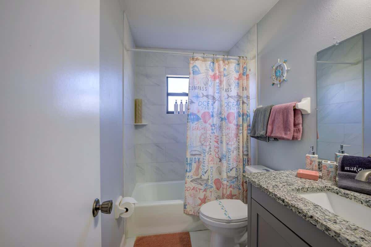 A bathroom with a shower curtain featuring nautical designs, a white toilet, a granite countertop, and a mirror with a towel rack.