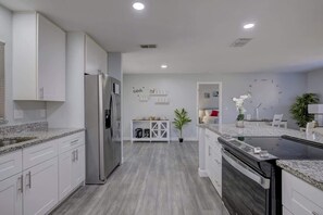 A modern kitchen with white cabinets, a stainless steel refrigerator, a built-in dishwasher, and a granite countertop. - Family Fun: Ping Pong, Bbq, Walk to Park Nearby (Sarasota)