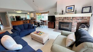 A spacious living room with a fireplace, a dining area, and a kitchen in the background. - Fv43 Bretton Woods Single Level Home With AC on Golf Course! (Rye)