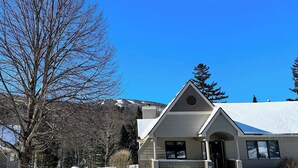 A house with a snow-covered roof, a front porch, and a mountain backdrop. - Fv43 Bretton Woods Single Level Home With AC on Golf Course! (Rye)