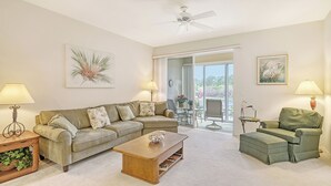 Ein Wohnzimmer mit einer Couch, Couchtisch und Sesseln, einem Deckenventilator und Blick auf eine Außenpatio-Terrasse.