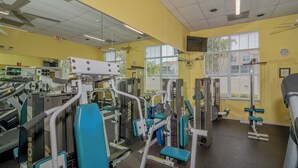 Ein Fitnessstudio mit verschiedenen Trainingsgeräten, einer Uhr und Fenstern mit Jalousien.