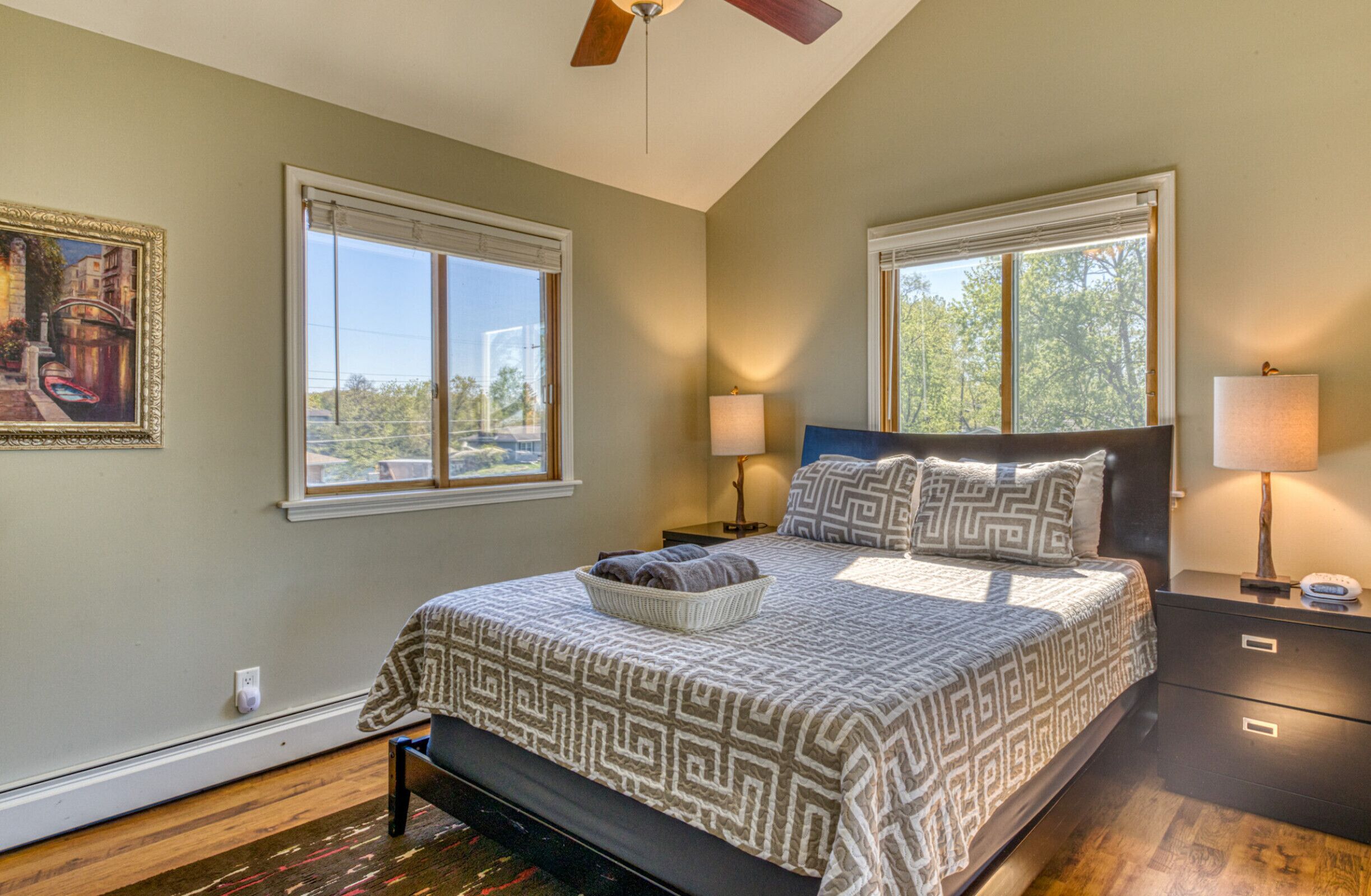 A bedroom with a large bed, two bedside lamps, a nightstand, and a ceiling fan.