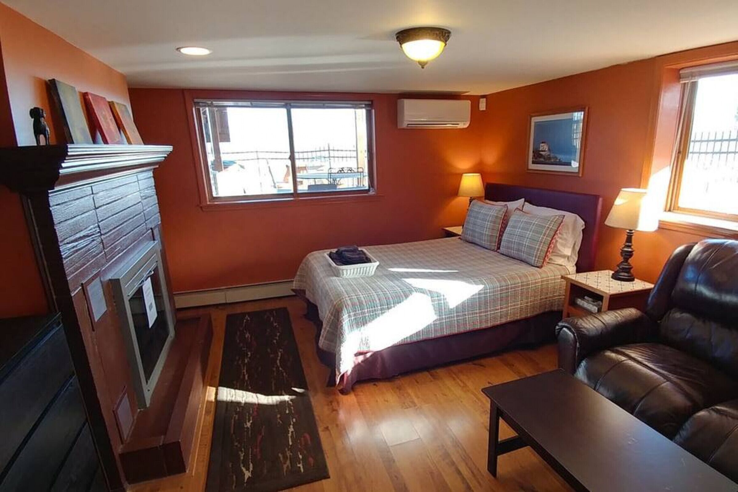 A cozy bedroom with a bed, two bedside tables, a lamp, a fireplace, and a window.