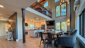 A spacious kitchen with a central island, a dining area with modern chairs, and a large window providing a view of the outdoors. - Elyon Hall + Coach House (Gary)