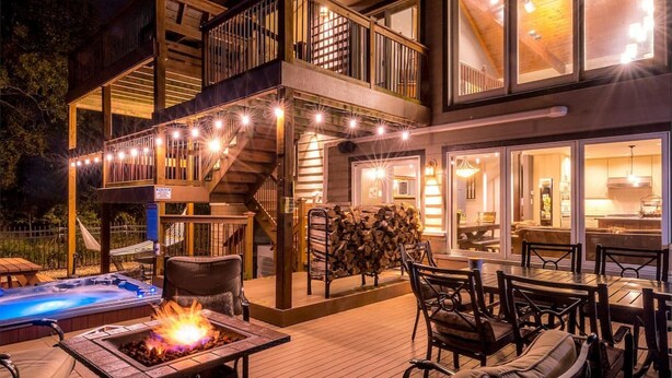 A two-story outdoor deck with a hot tub, seating area, and a fire pit. - Elyon Hall + Coach House (Gary)
