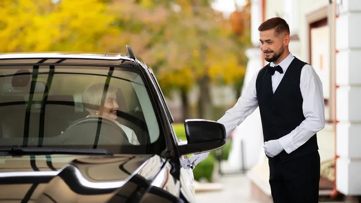 A person in a black vest and white shirt standing next to a car.