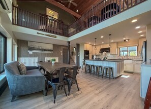 Une cuisine spacieuse dotée d’un îlot central, un coin repas avec un canapé et des chaises, et un balcon au deuxième étage avec une balustrade.