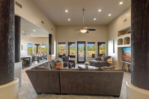 A spacious living area with a large sectional sofa, a ceiling fan, and a view of the outdoors through large windows. - Gamble (Scottsdale)
