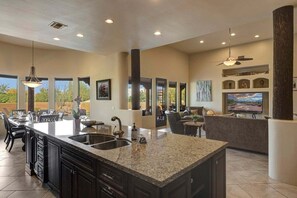 A spacious kitchen with a large island, dark cabinetry, and a dining area with a view. - Gamble (Scottsdale)
