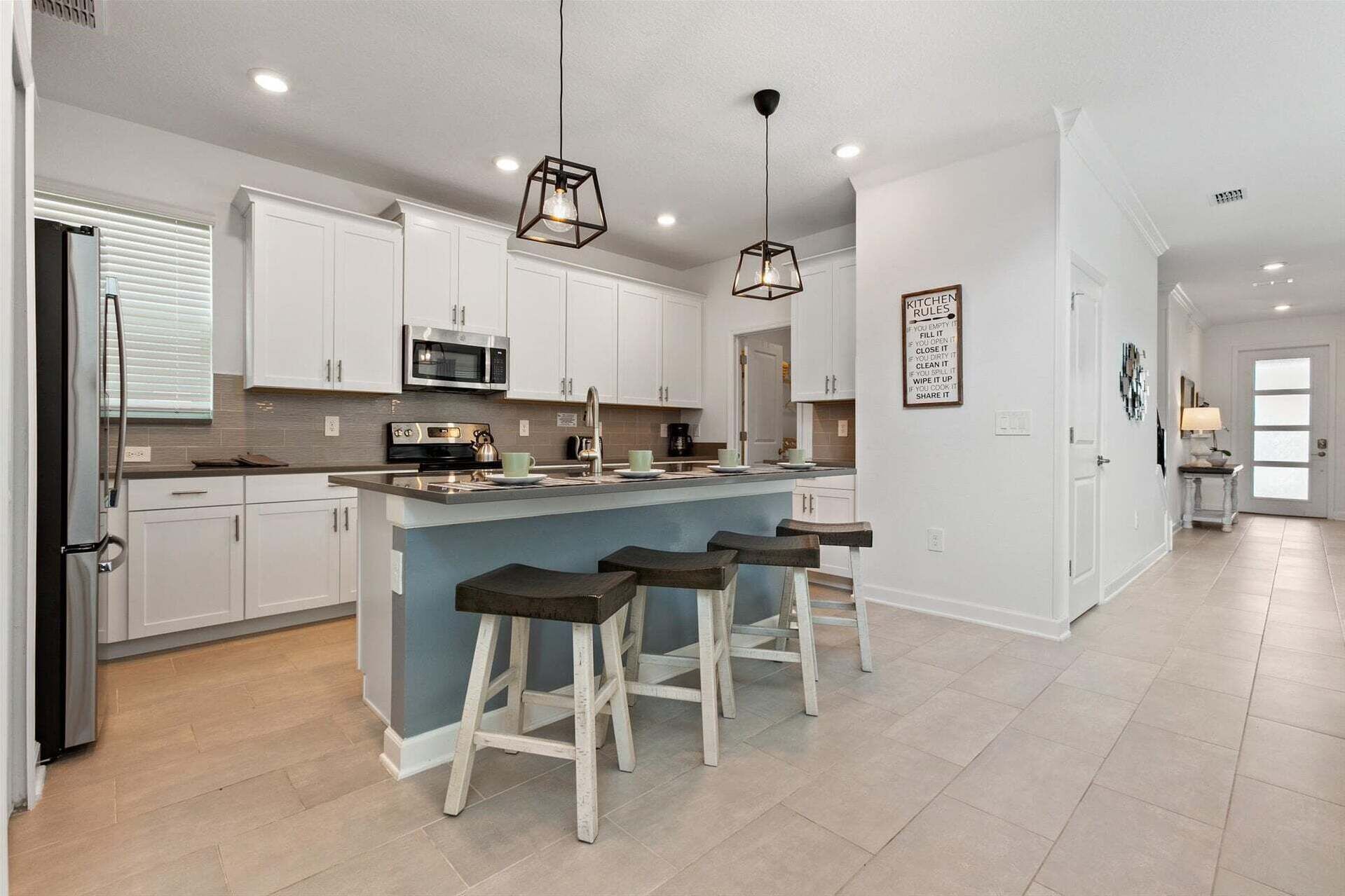 A modern kitchen with white cabinets, a central island with stools, a microwave, and a coffee maker.