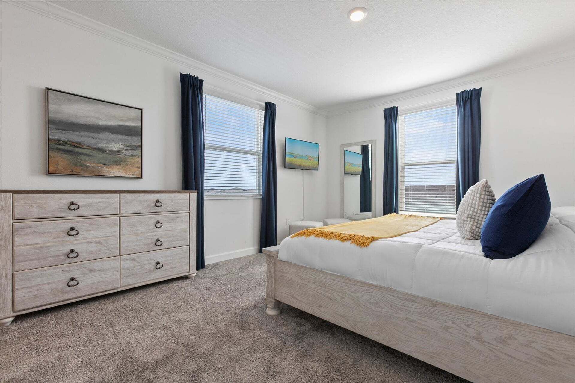 Een slaapkamer met een bed, een dressoir, een schilderij en een raam met gordijnen.
