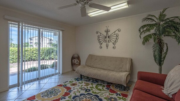 Ein Wohnzimmer mit einer Couch, einem roten Sessel, einem gemusterten Teppich, einem Wandbild und einem Deckenventilator.