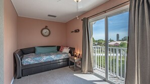 Ein Schlafzimmer mit einem großen Schiebeglasfenster zum Balkon, einem Bett mit gemusterten Bettbezügen, einer Wanduhr und einem kleinen Tisch mit Lampe.