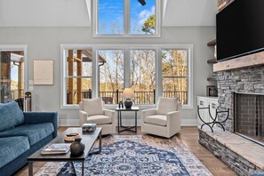 A living room with a fireplace, large windows, a sofa, two armchairs, and a coffee table. - Lakeside Haven With Gourmet Kitchen (Hartwell)