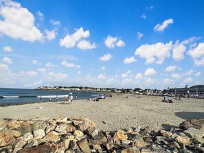 A beach with rocky foreground, a clear sky, and distant buildings. - Kurtz Cottage - Y856 (York Beach)