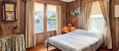 Een kamer met houten wanden, een bed, een tafel met een lamp en een plafondventilator.