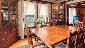 A dining room with a wooden table and chairs, a bookshelf, and a view of the outdoors. - Kurtz Cottage - Y856 (York Beach)