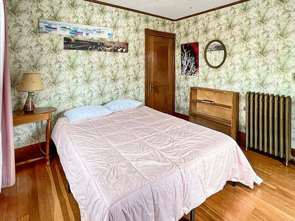 Un dormitorio con cama, mesita de noche, cómoda, radiador y papel tapiz floral.