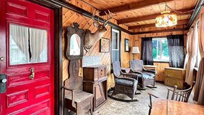 A wooden interior with a red door, a mounted deer head, wicker furniture, and a chandelier. - Kurtz Cottage - Y856 (York Beach)