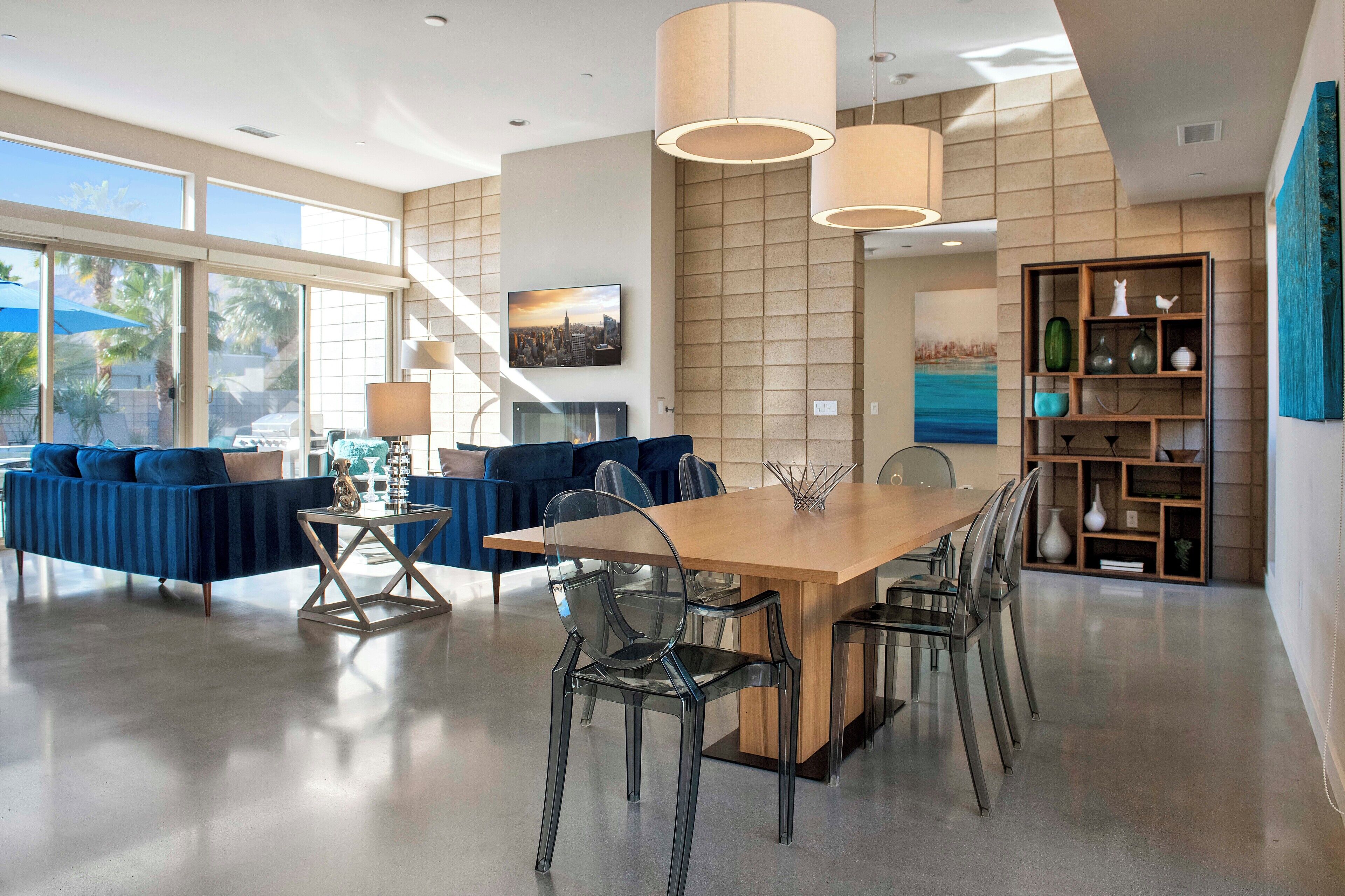 A spacious living area with a large wooden dining table, clear glass chairs, and a blue sofa.