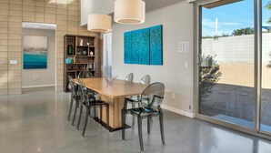 A modern dining area with a wooden table, clear chairs, and pendant lights. - Lucent (Palm Springs)