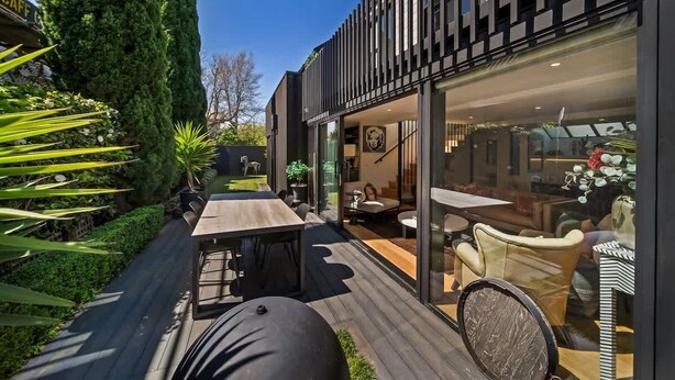 Ein modernes Gebäude mit einer Terrasse, die ein Holzdeck, Sitzgelegenheiten im Freien und einen Glasvordereingang bietet.