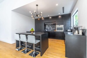 A modern kitchen with a central island, bar stools, a chandelier, and a large window. - Lux Villa With Pool Wynwood House by Rovetravel (Miami)
