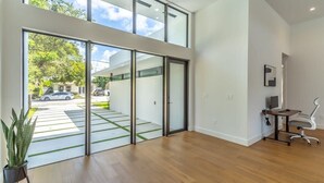 Un intérieur moderne avec de grandes portes vitrées donnant sur un espace extérieur abrité, un bureau avec une chaise et une plante en pot.