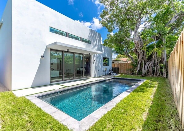 Une maison moderne dotée d’une piscine, d’un patio couvert et d’une clôture en bois.