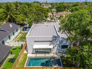Une maison moderne à deux étages avec une piscine, entourée d’une végétation luxuriante et de palmiers.