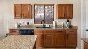 A kitchen with granite countertops, wooden cabinets, a dishwasher, a coffee maker, and a window with blinds. - Glendale w Pool & Games (Glendale)