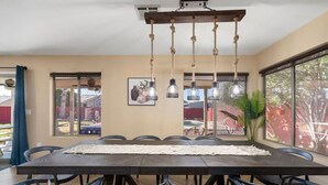 A dining area with a large table, chairs, pendant lights, and a view of the outdoors. - Glendale w Pool & Games (Glendale)