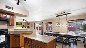 A kitchen with granite countertops, wooden cabinets, a black stove, and a dining area with a long table and chairs. - Glendale w Pool & Games (Glendale)