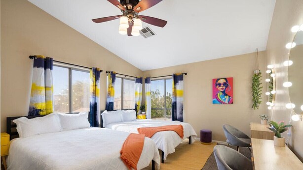 A hotel room with two beds, a ceiling fan, a desk with a chair, and a large window with curtains. - Glendale w Pool & Games (Glendale)