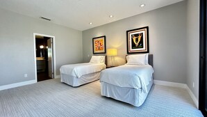 A hotel room with two single beds, a bedside table with a lamp, a framed picture on the wall, and a door leading to a bathroom.